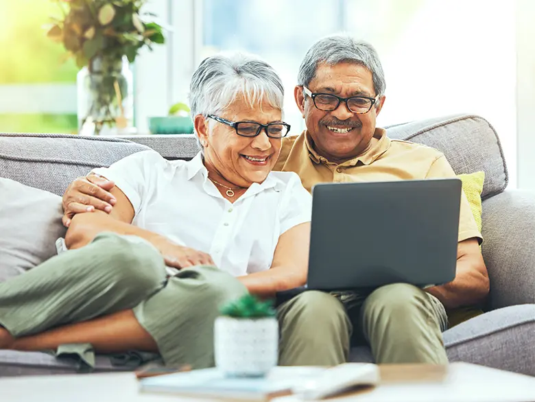 An elderly couple sitting together with a laptop on the husband's lap