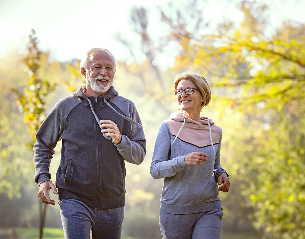 An elderly couple running outdoors together.