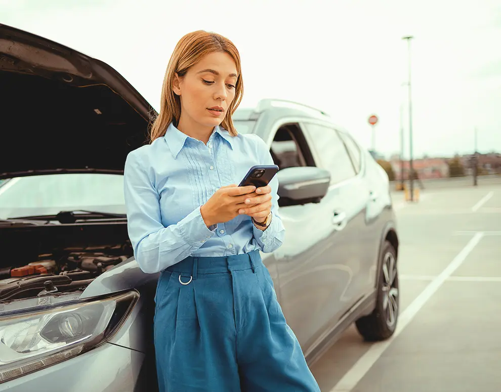 Person standing next to a car with the hood open, using a smartphone, researching GAP Plus coverage from ICCU.